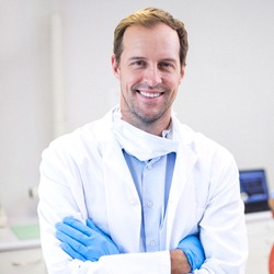 A dentist smiling while a patient has their teeth checked by a dental hygienist