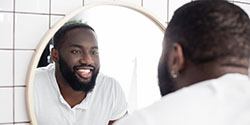 Man smiling at white, straight, healthy teeth in mirror