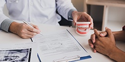 Dentist holding model of teeth and reviewing types of dentures