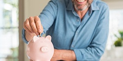 man putting coins into a pink piggy bank 