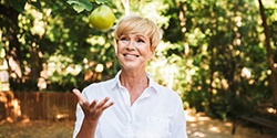 Woman tossing green apple into the air outside