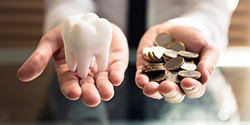 Hands holding a fake tooth model and golden coins