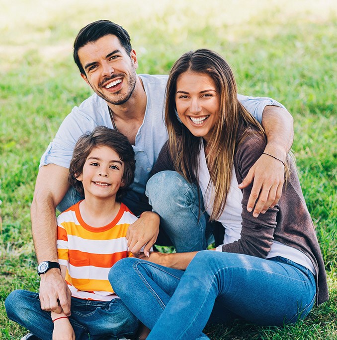 Family of three sitting outdoors smiling