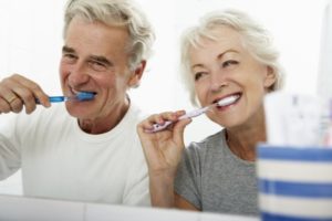 senior man and woman brushing their teeth to become good dental implant candidates 