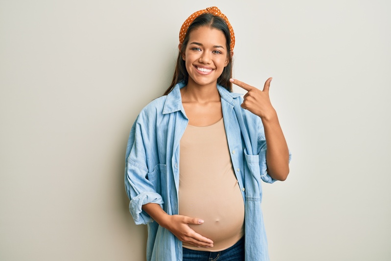 A woman experiencing pregnancy pointing to her smile