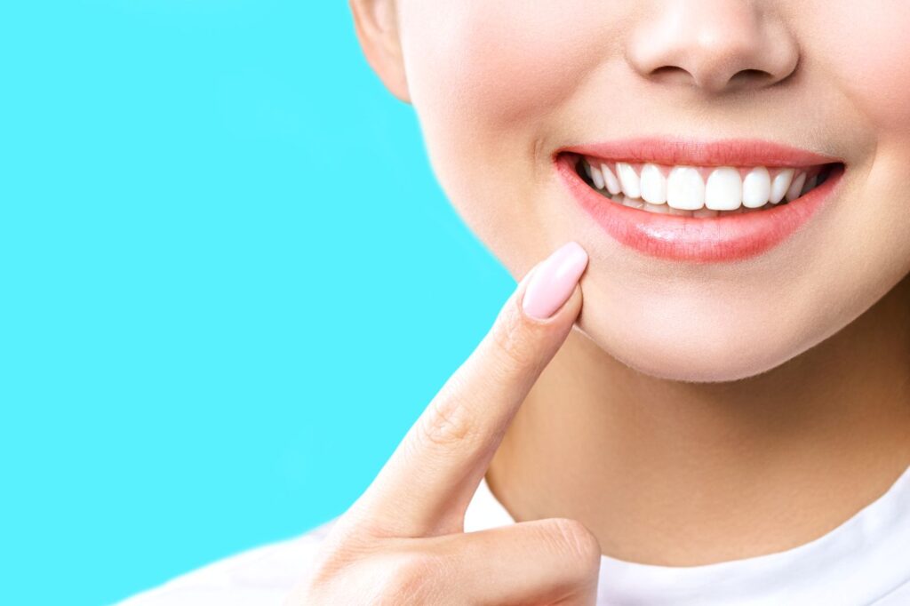 Nose-to-shoulder view of woman pointing to her bright smile with one finger