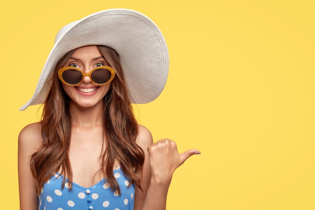 Woman in polka dot top and floppy hat smiling while pointing to the side with her thumb