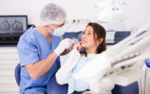 Middle-aged woman pointing at her teeth while dentist prepares to examine her smile